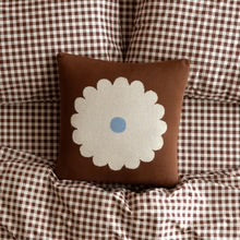 Brown decorative throw pillow with a white scalloped flower design and blue center.