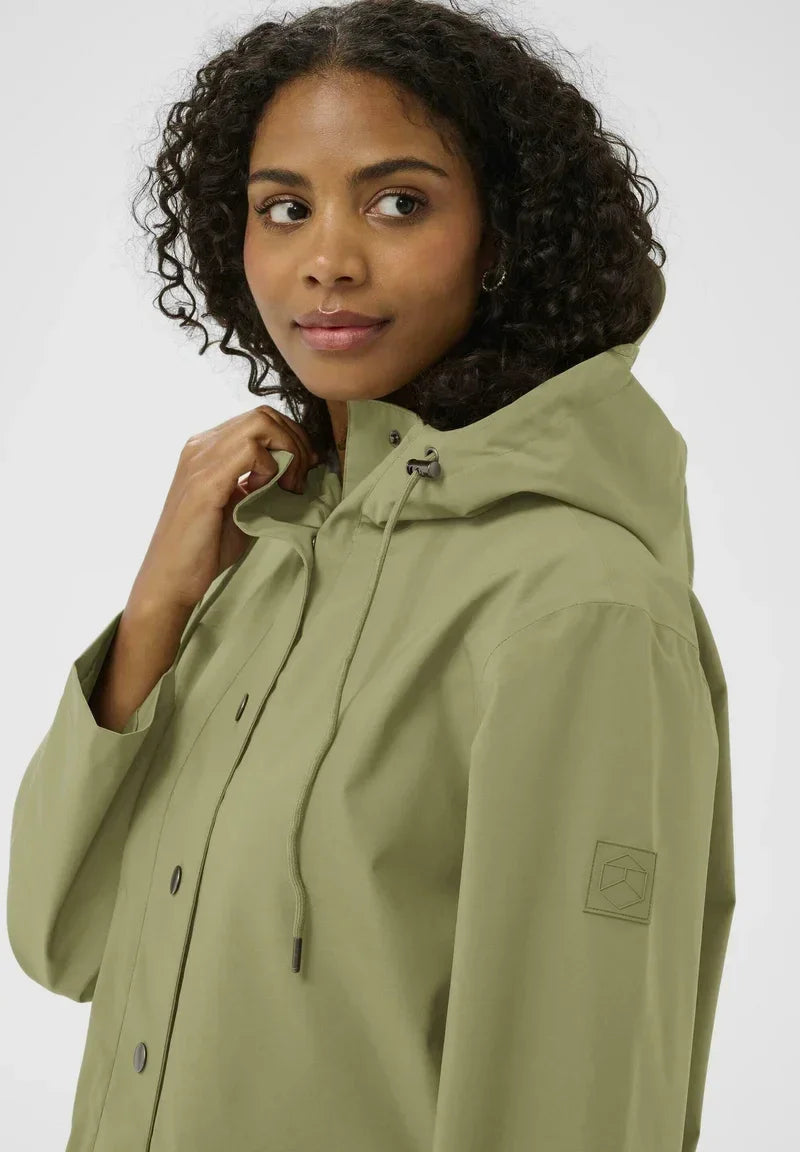 Woman in olive green hooded raincoat with drawstring, button front, and sleeve patch detail
