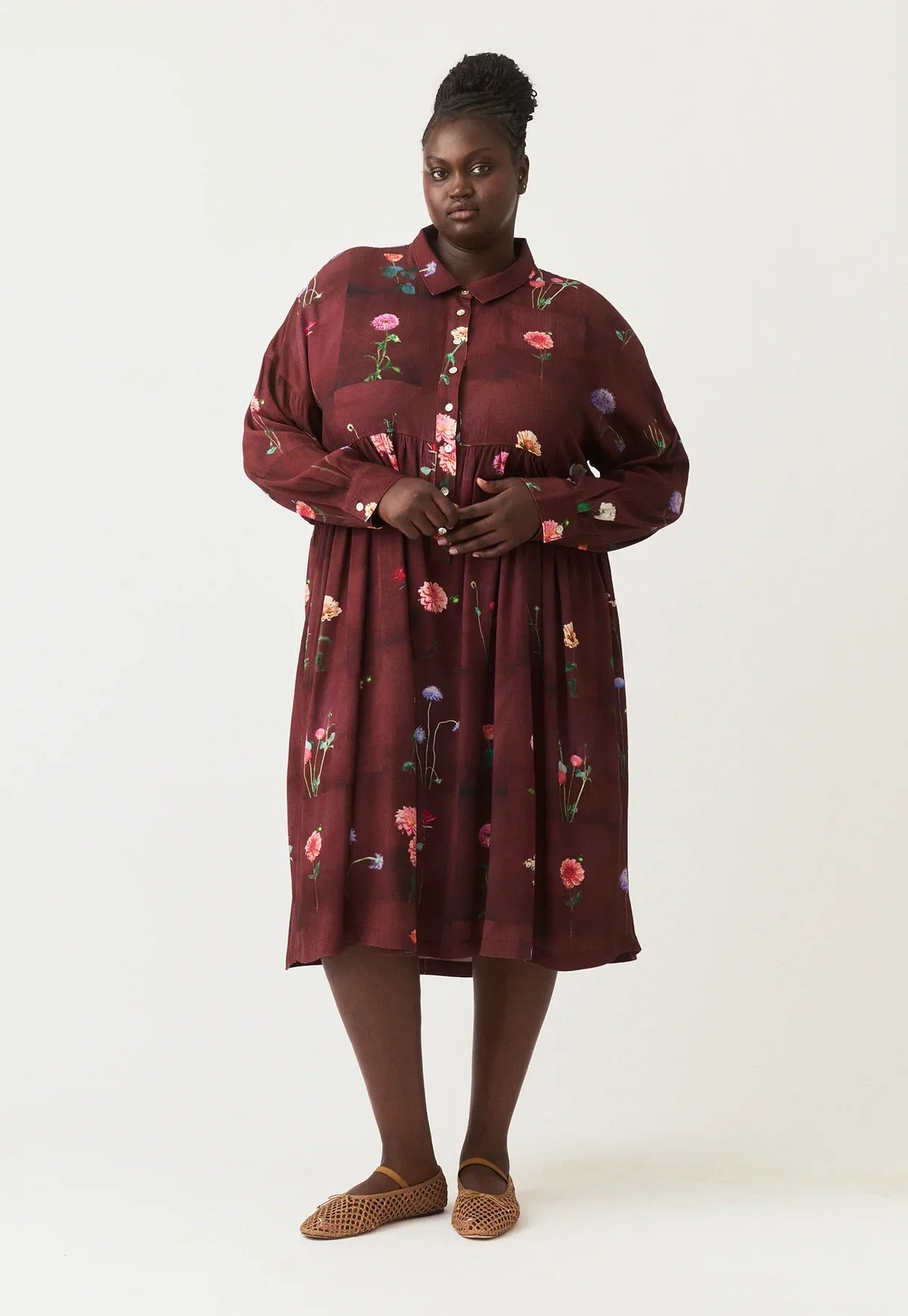Plus size woman in burgundy floral shirt dress with long sleeves and button front, styled with woven flats