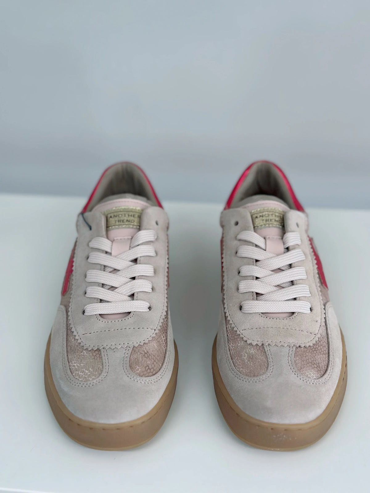 Pair of beige Another Trend sneakers with red accents and white laces.