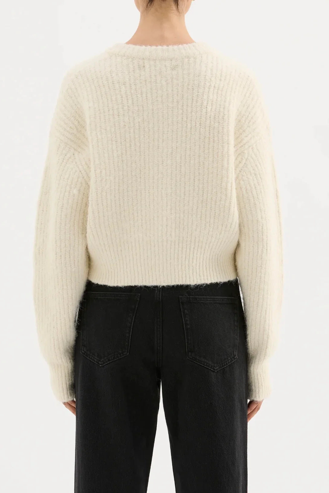 Back view of woman wearing cream ribbed knit sweater and high-waisted black jeans