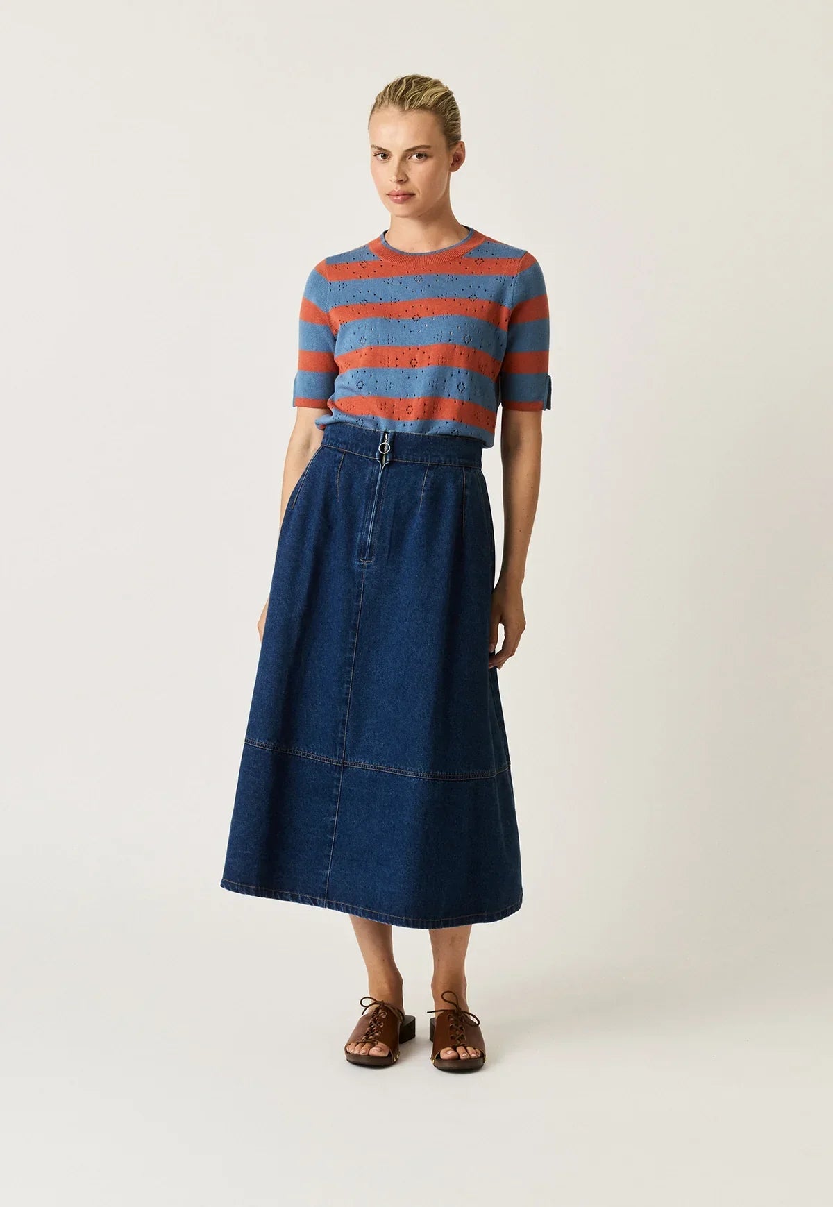 Woman wearing a NANCYBIRD Aries Denim Skirt in dark wash with a striped top and brown sandals.