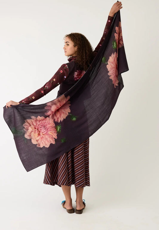 Woman wearing floral print scarf and striped skirt, holding scarf wide against white background