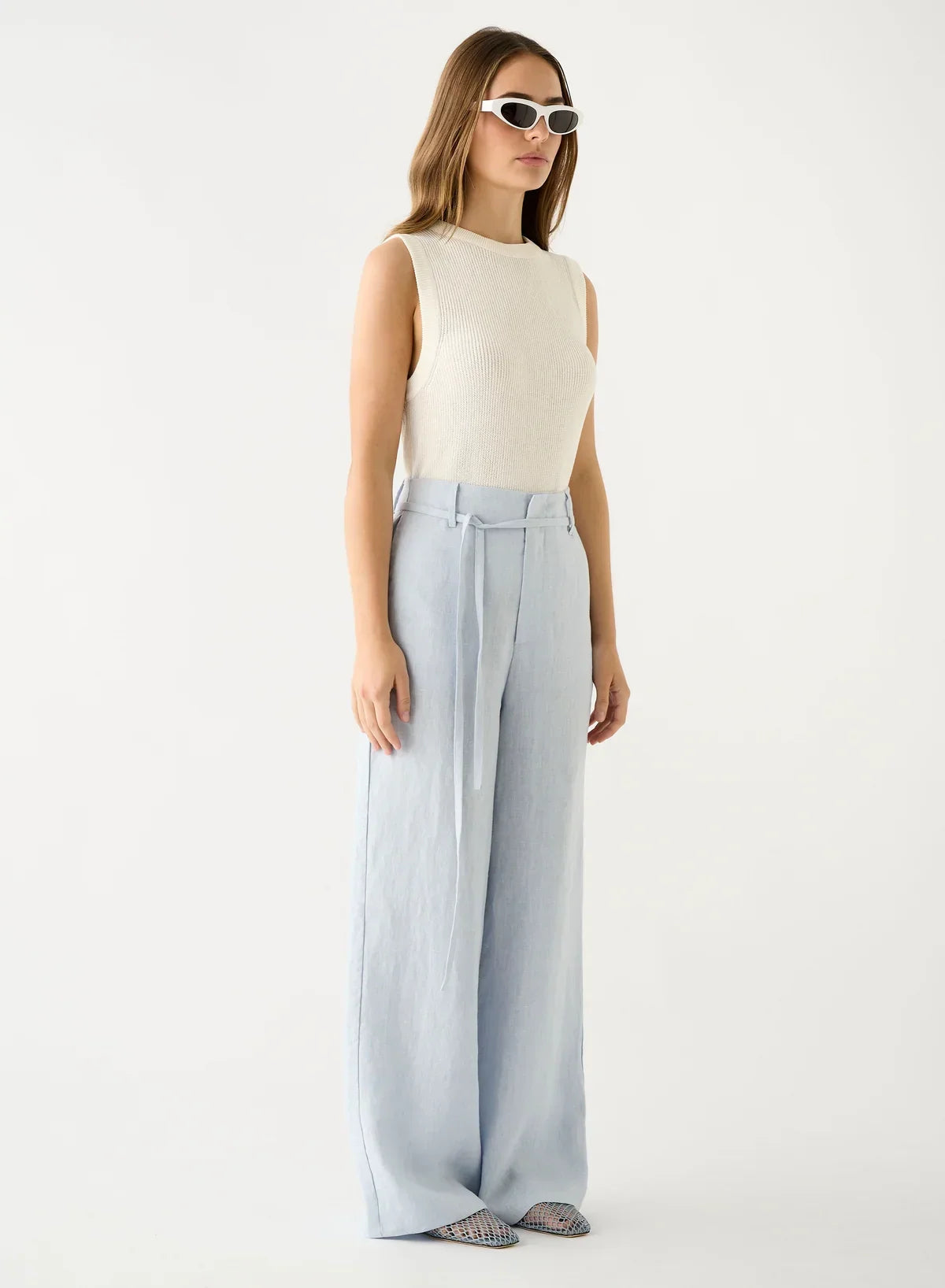 Model wearing Esmaee Olivia Pant in Ice Blue with a white sleeveless top and white sunglasses.