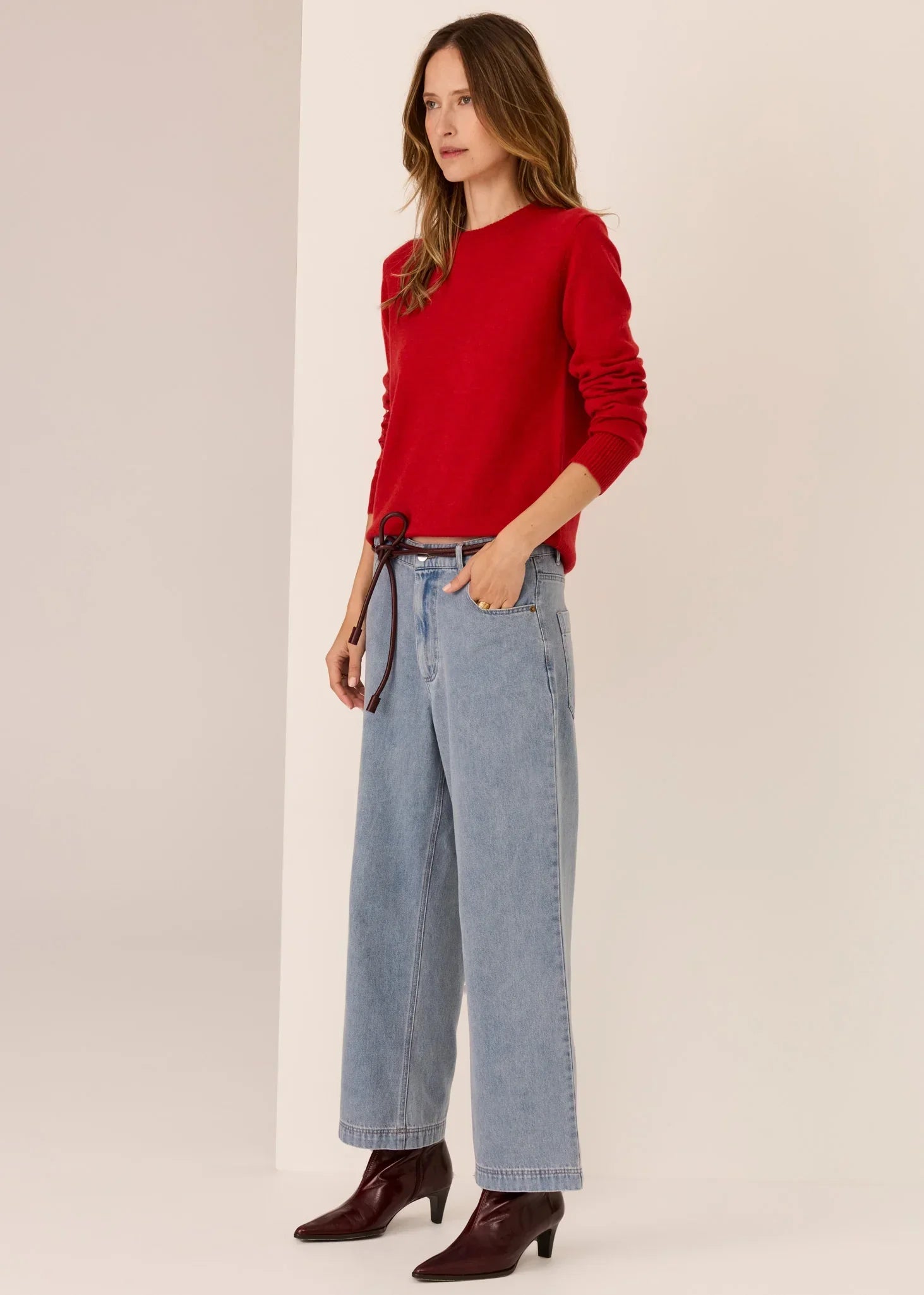 Woman in red sweater, wide-leg blue jeans, and ankle boots in a minimalist studio