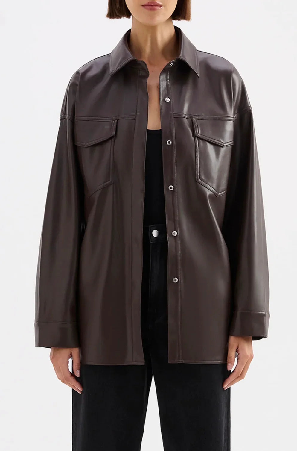 Brown leather shirt jacket with front pockets and button closure, styled with black pants