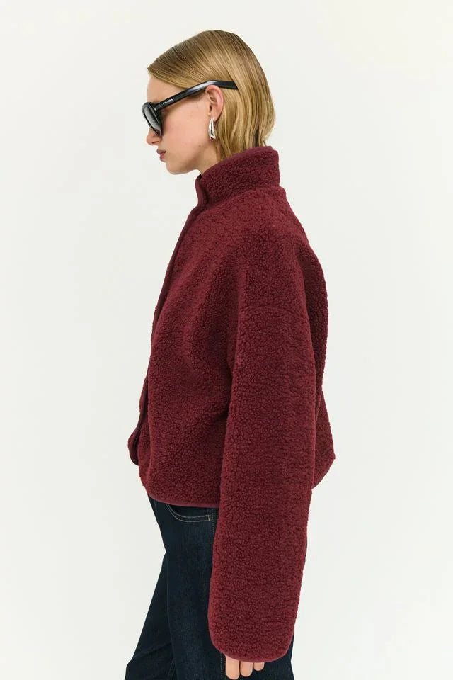 Woman wearing burgundy teddy fleece jacket, sunglasses, and jeans — cozy women's fashion