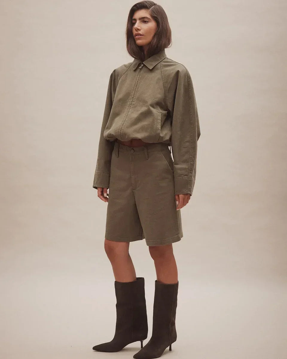 Woman wearing Nobody Denim Rowan Bermuda Shorts in Safari with a matching olive jacket and boots.