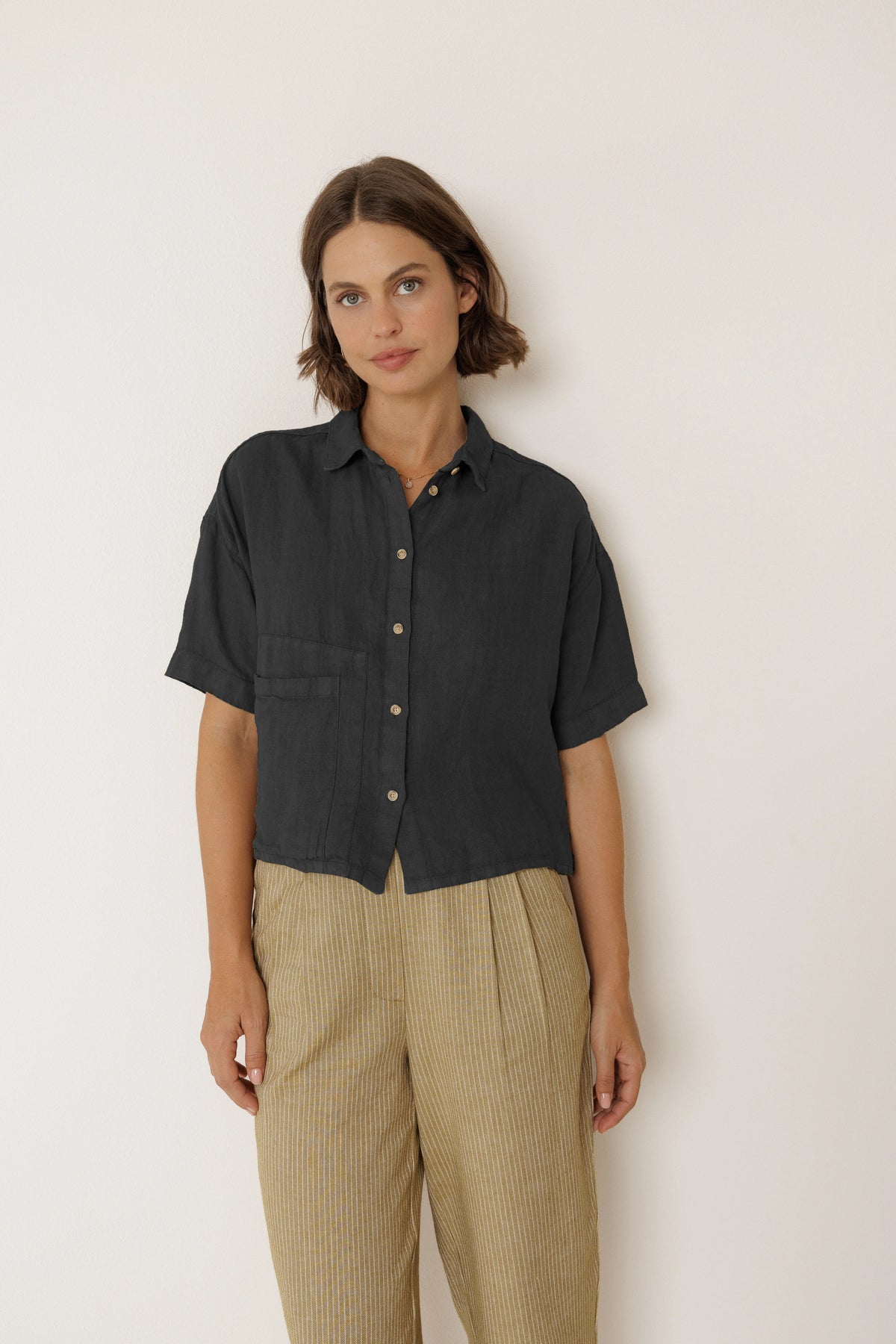 Woman wearing an INDI & COLD Crop Linen Shirt in Carbon with tan striped trousers