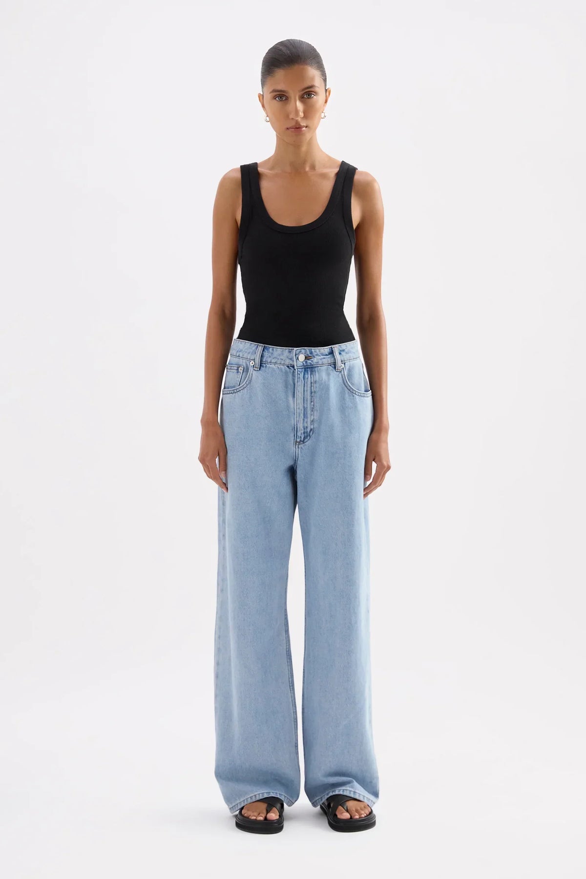 Woman wearing a Nude Lucy Organic Rib Singlet in Black and light blue wide-leg jeans.