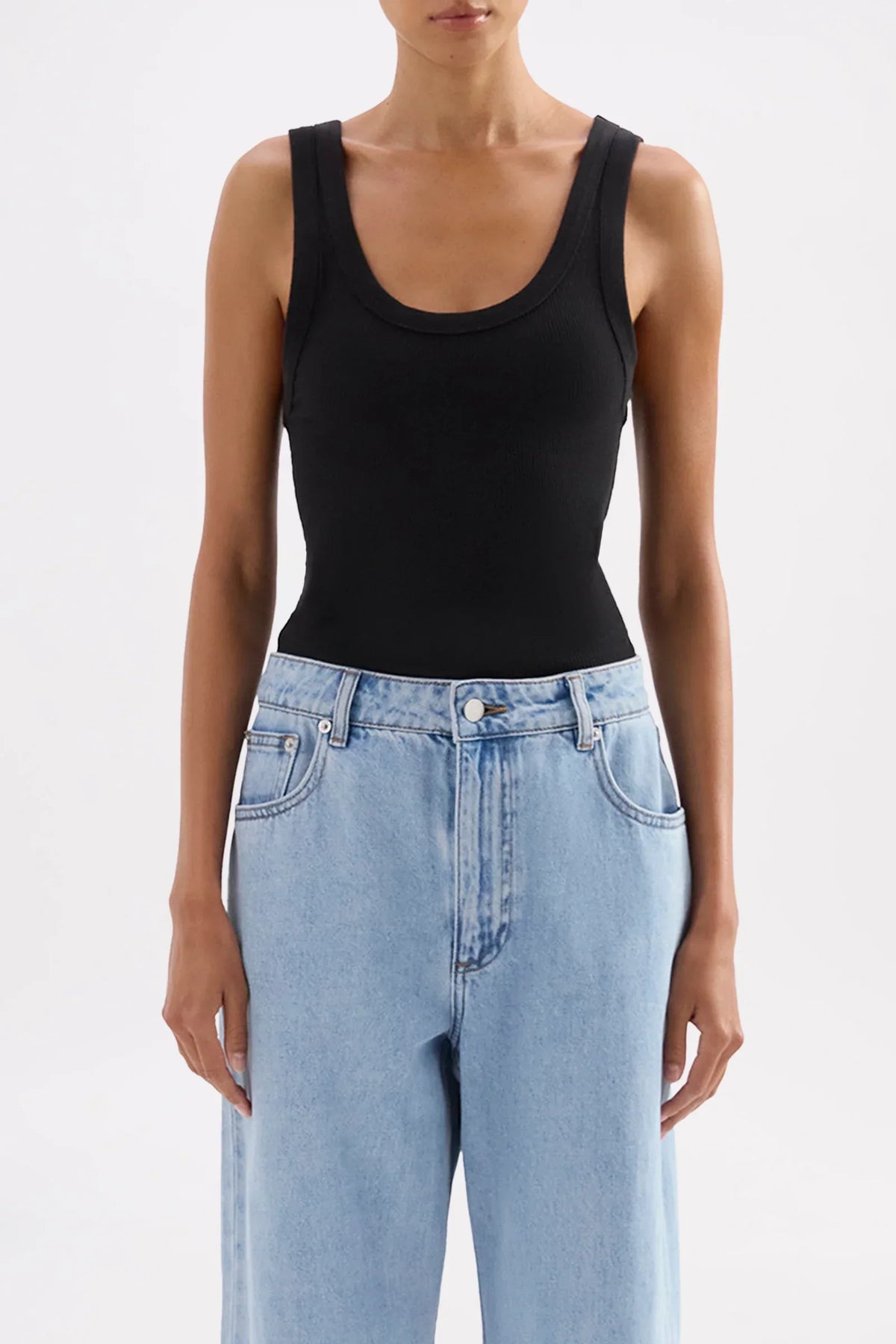Woman wearing a Nude Lucy Organic Rib Singlet in black and light blue jeans.