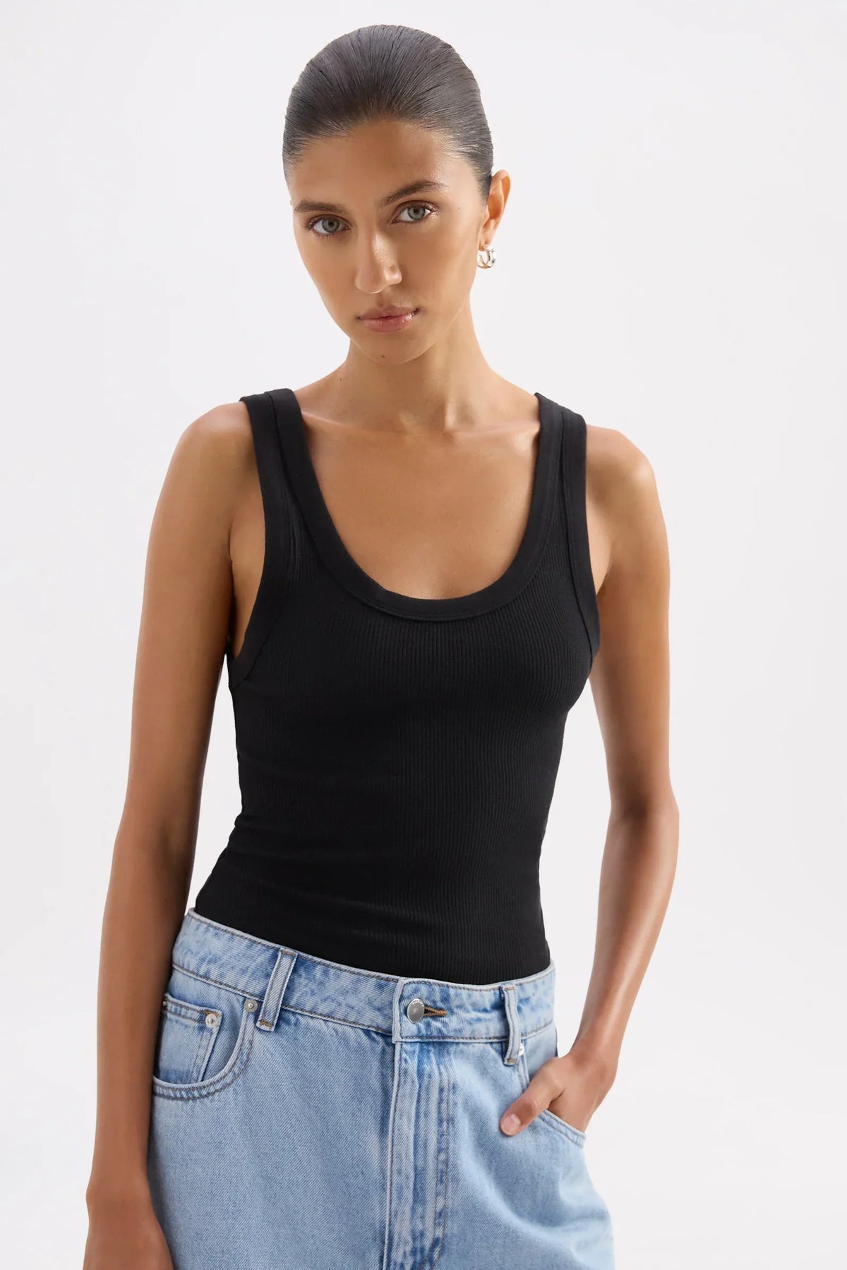 Woman wearing a Nude Lucy Organic Rib Singlet in black paired with blue jeans.