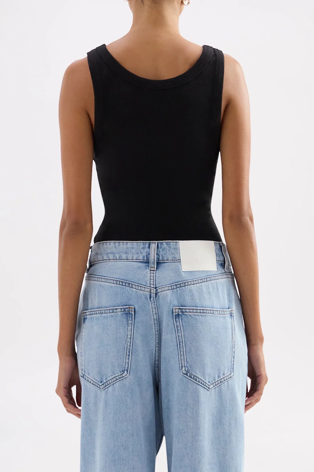 Back view of a woman wearing a Nude Lucy Organic Rib Singlet in black and light blue jeans.