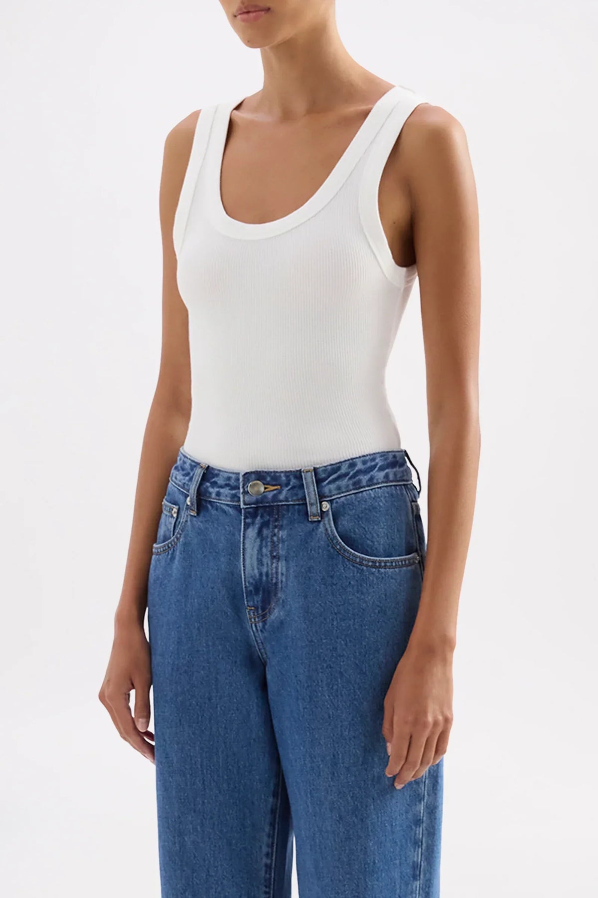 Woman wearing a Nude Lucy Organic Rib Singlet in white paired with blue jeans.