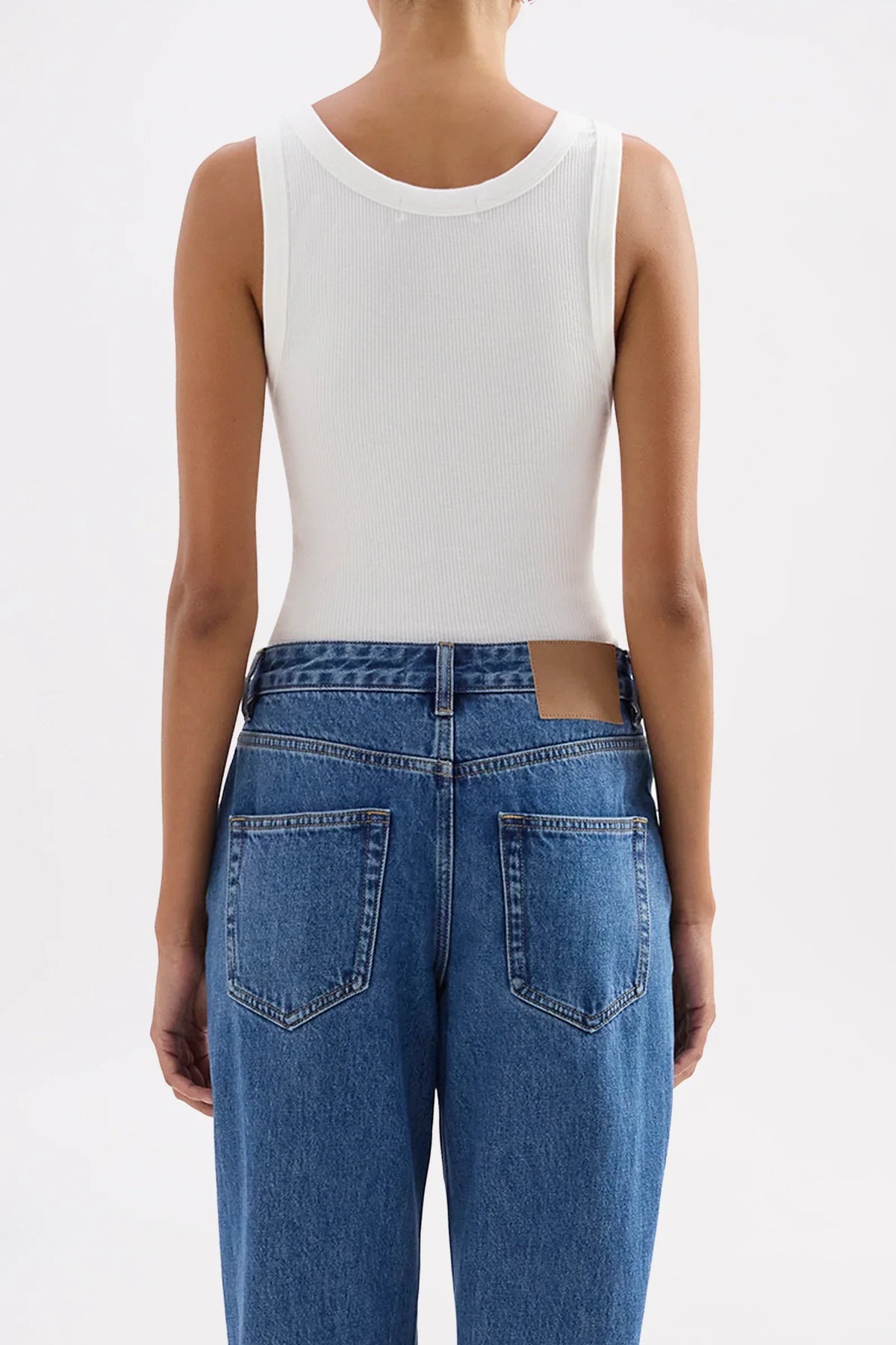 Back view of a model wearing a Nude Lucy Organic Rib Singlet in white and blue jeans.