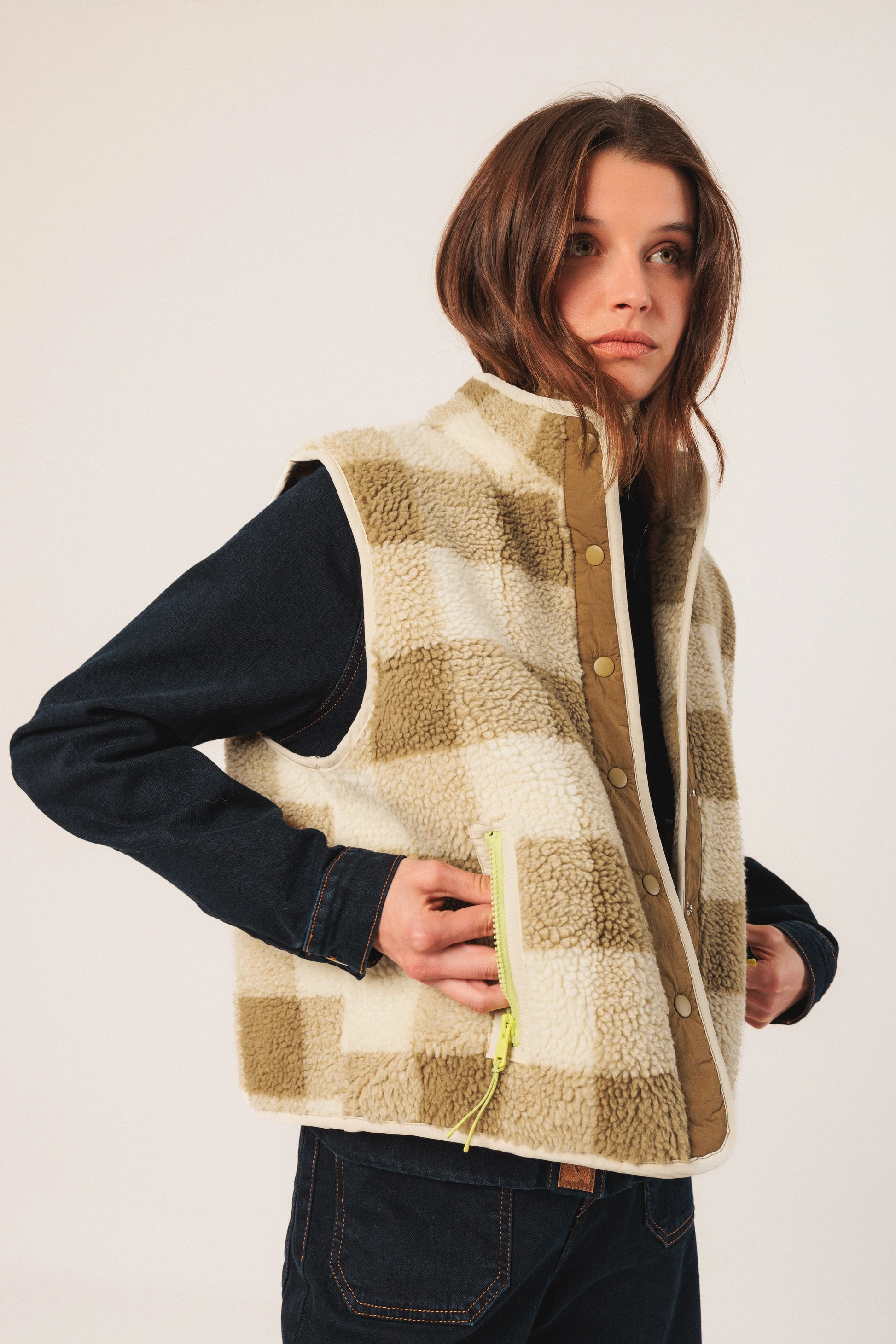 Woman wearing cozy shearling vest with neon zipper, layered over denim shirt and jeans