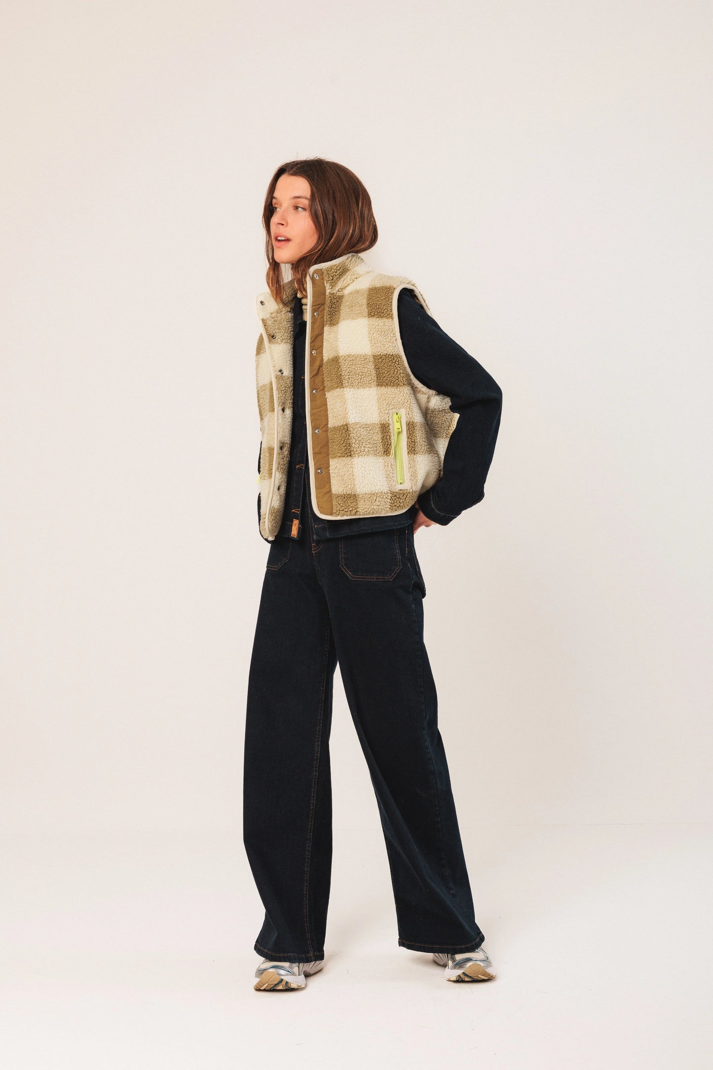 Woman in cozy plaid shearling vest, dark denim, and sneakers, styled for casual fashion.
