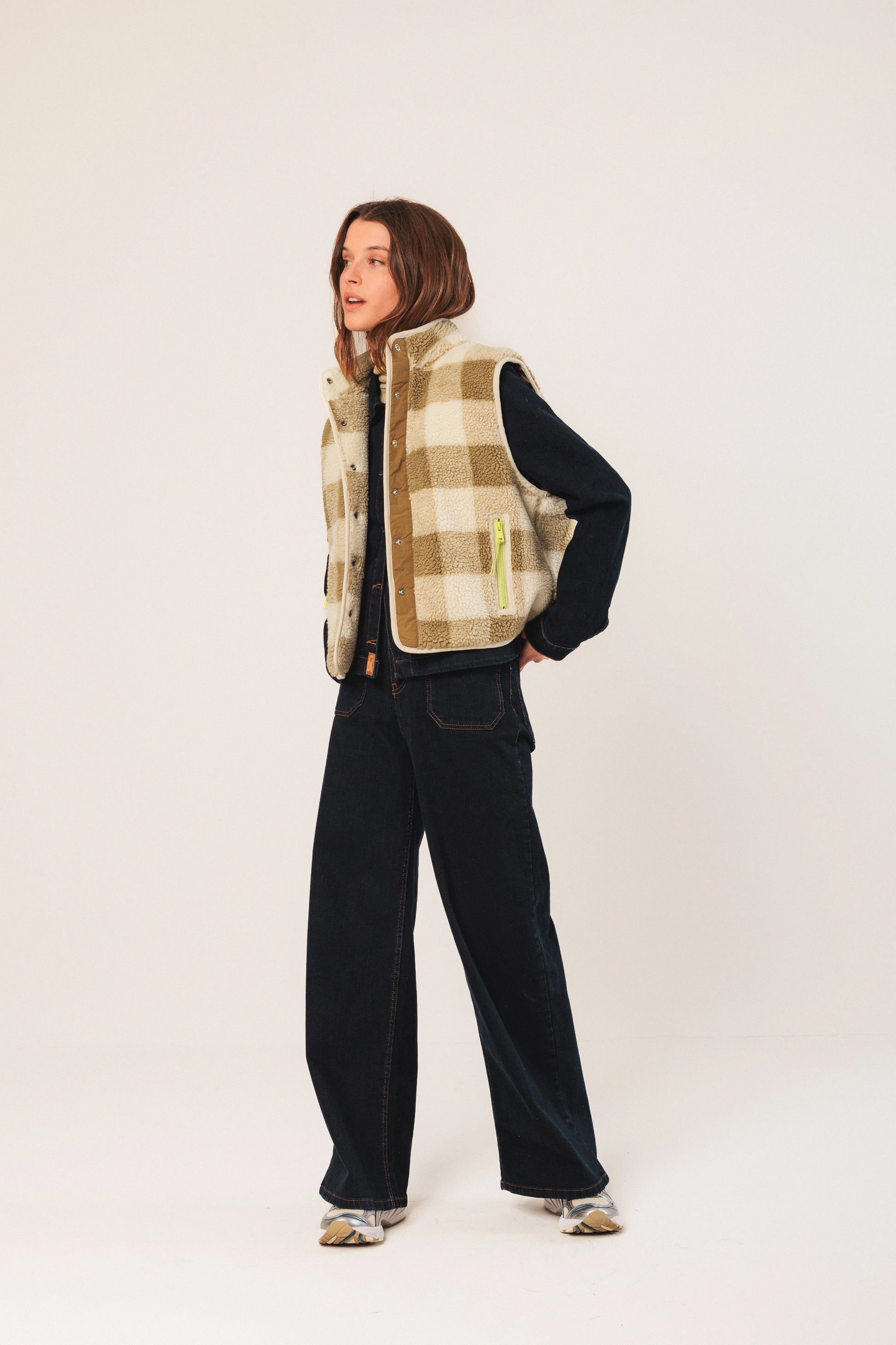 Woman in cozy plaid shearling vest, dark denim, and sneakers, styled for casual fashion.
