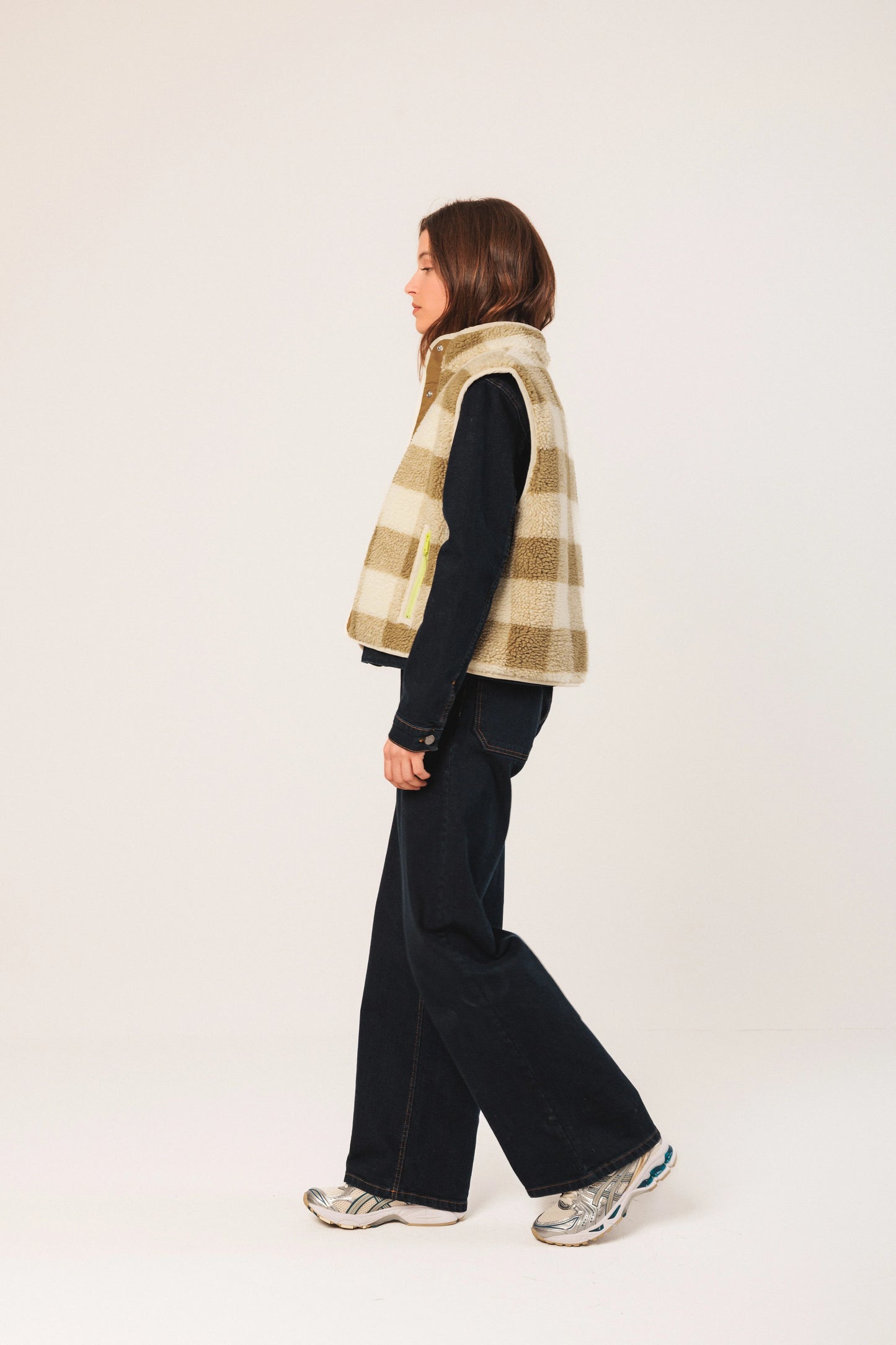 Woman in plaid shearling vest, denim shirt, wide-leg jeans, and silver sneakers
