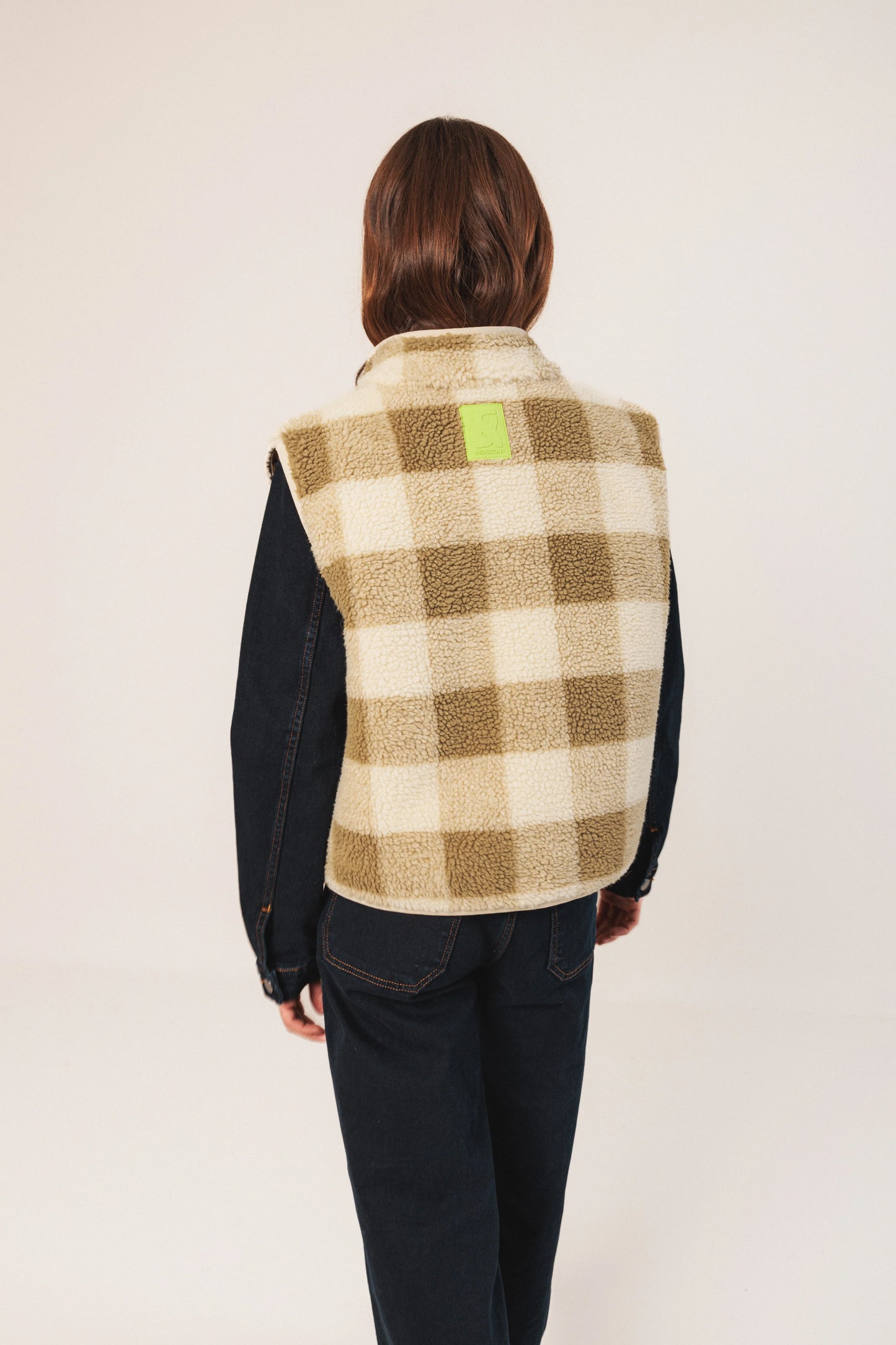 Woman wearing cozy plaid sherpa vest with denim sleeves, back view