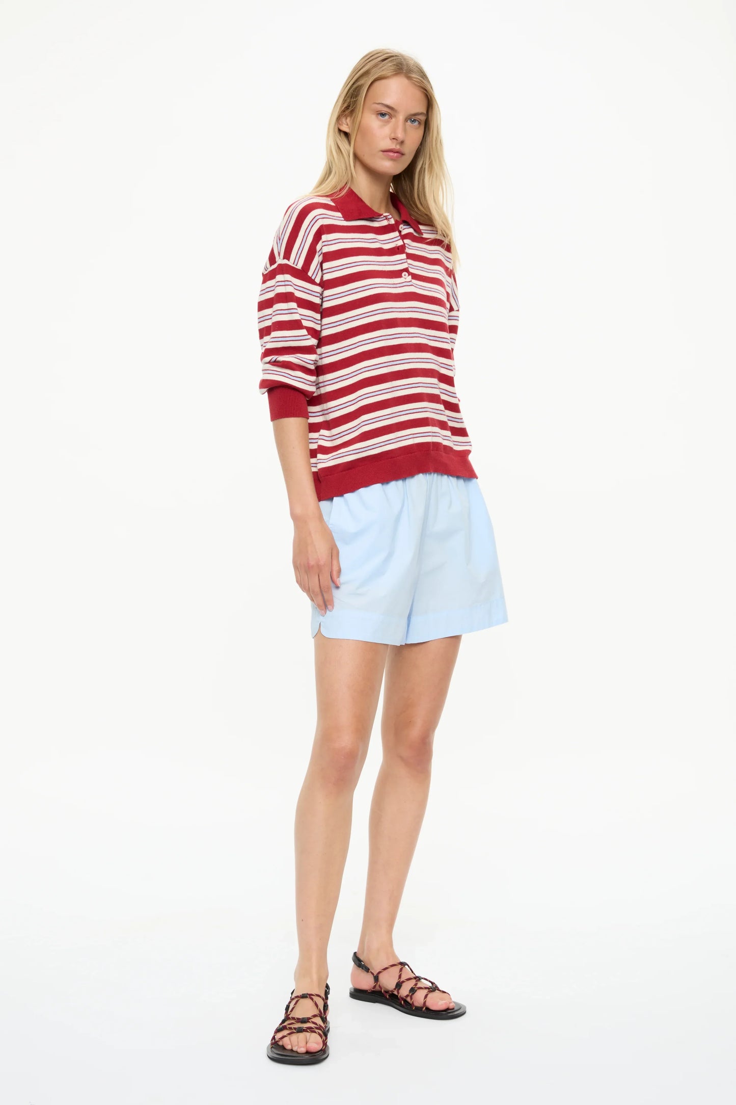 Woman in red and white striped polo shirt, light blue shorts, and strappy sandals