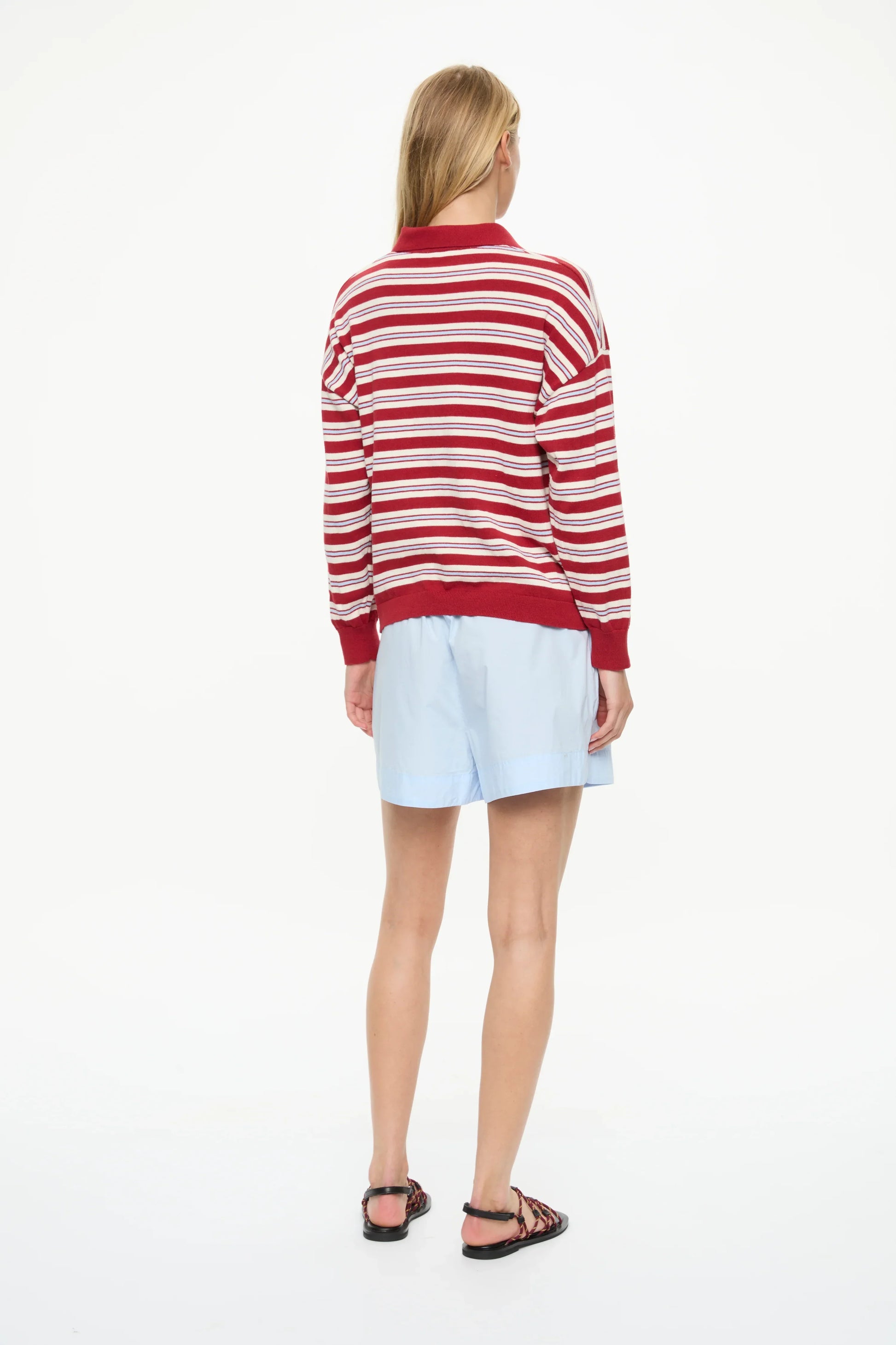 Woman in red and white striped polo sweater with light blue shorts and sandals, back view