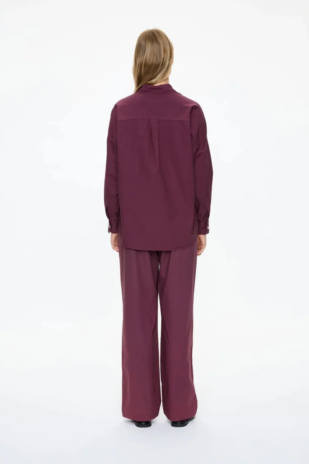 Back view of woman in burgundy long sleeve shirt and wide-leg pants, modern women's fashion
