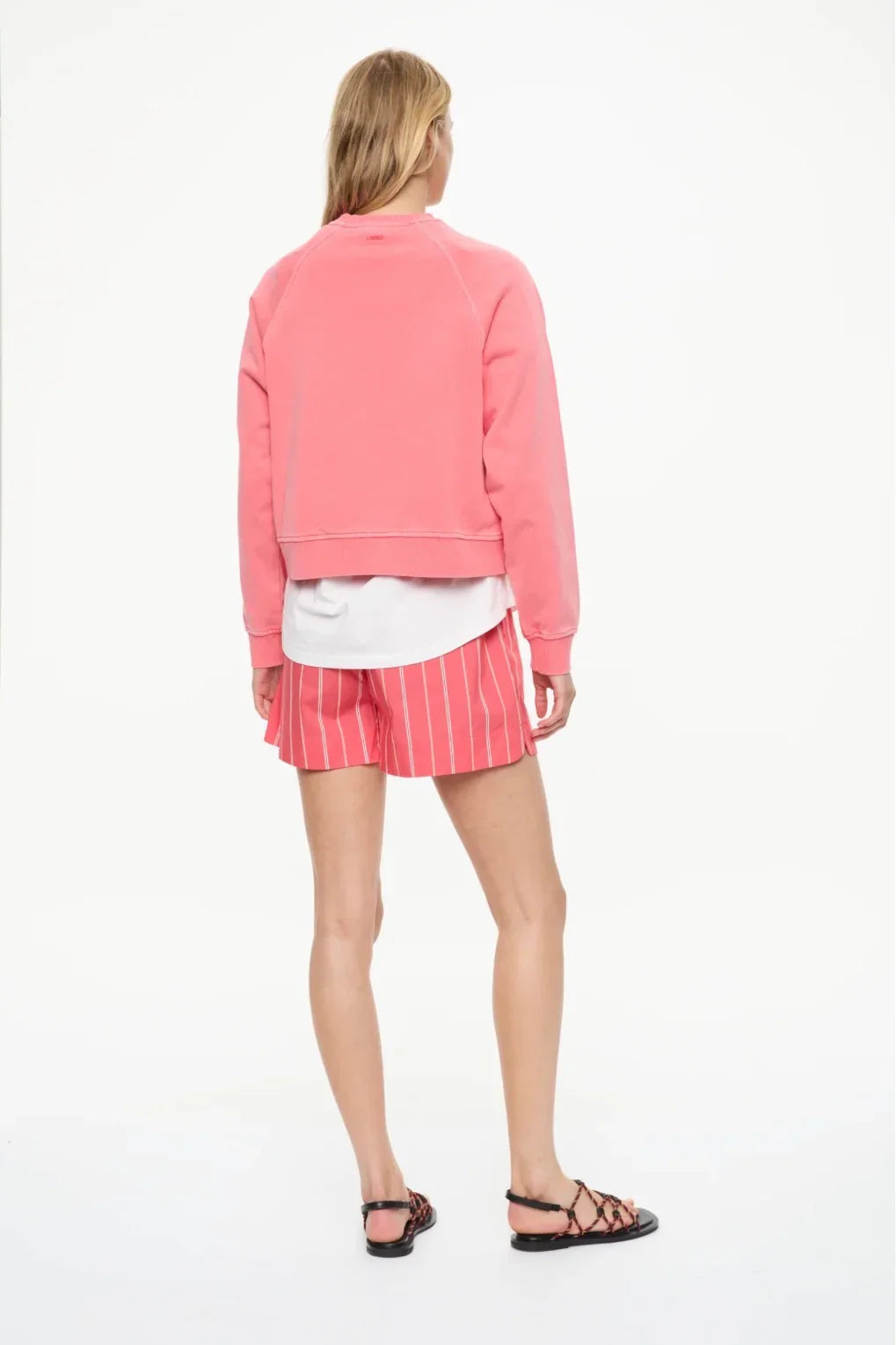 Woman wearing pink cropped sweatshirt, striped shorts, and strappy sandals, back view