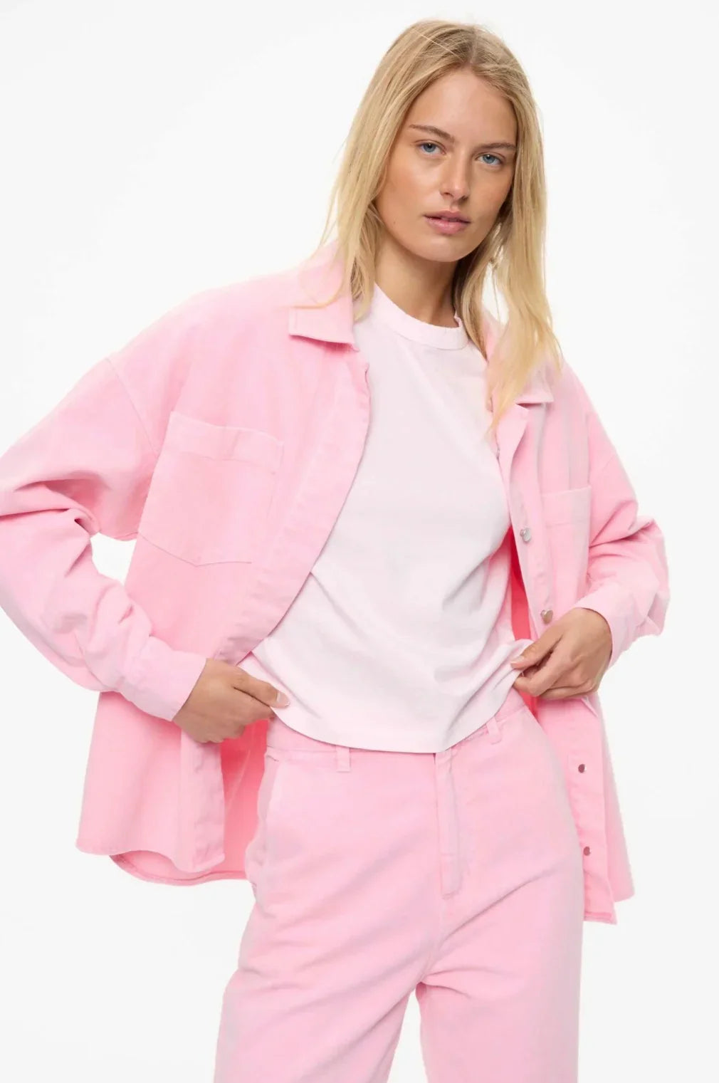 Woman in pink oversized shirt jacket and matching pants, styled with white tee, modern women's fashion