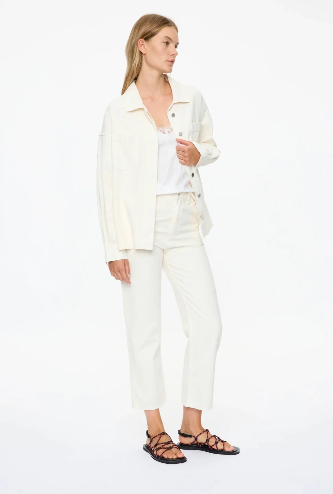 Woman in white denim jacket and matching pants, styled with strappy sandals for a chic, casual look