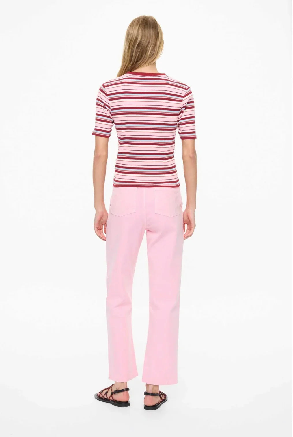 Woman wearing striped pink and red tee with light pink pants and sandals, back view