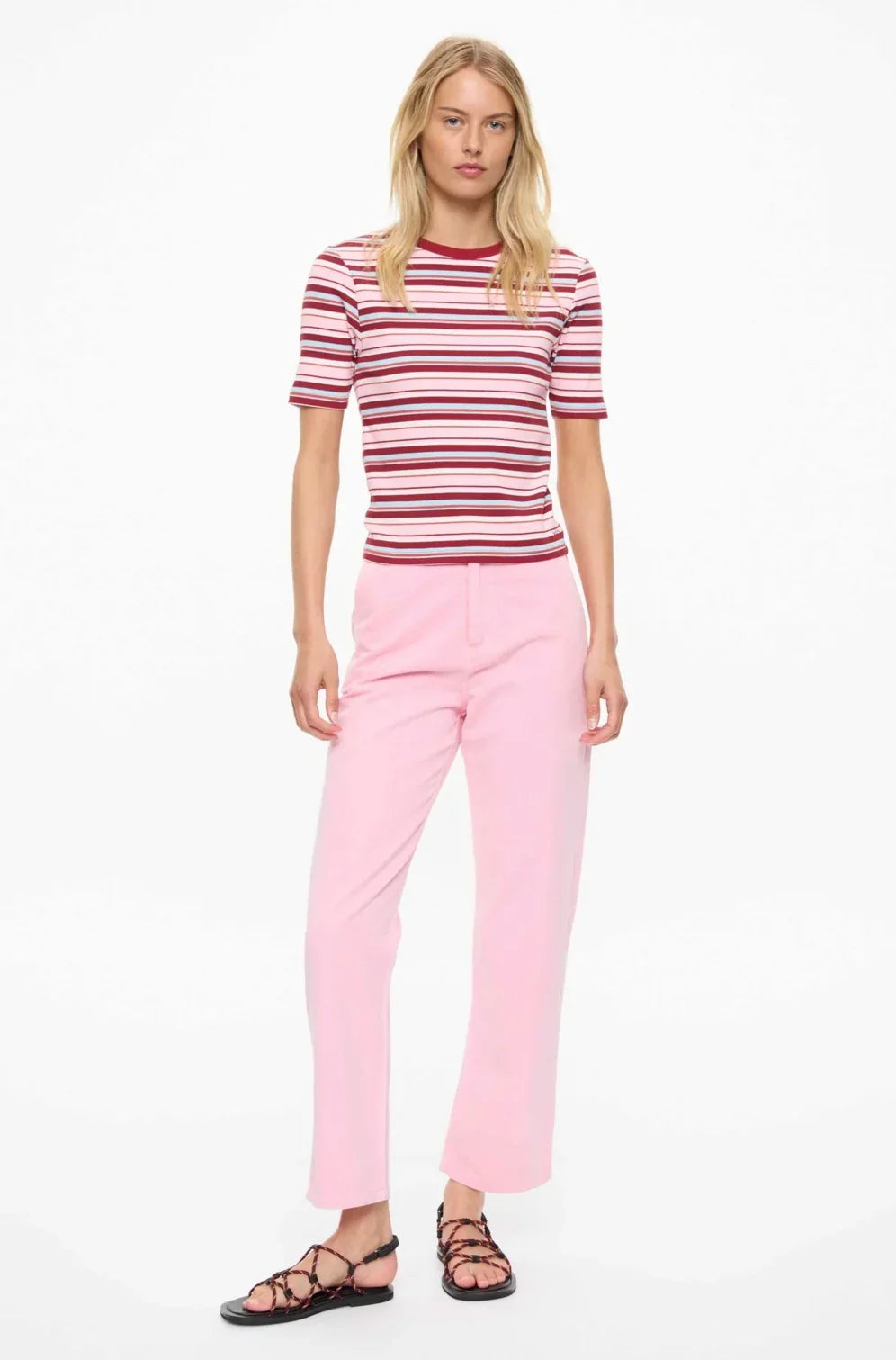 Woman wearing striped pink and red top with light pink pants and strappy sandals