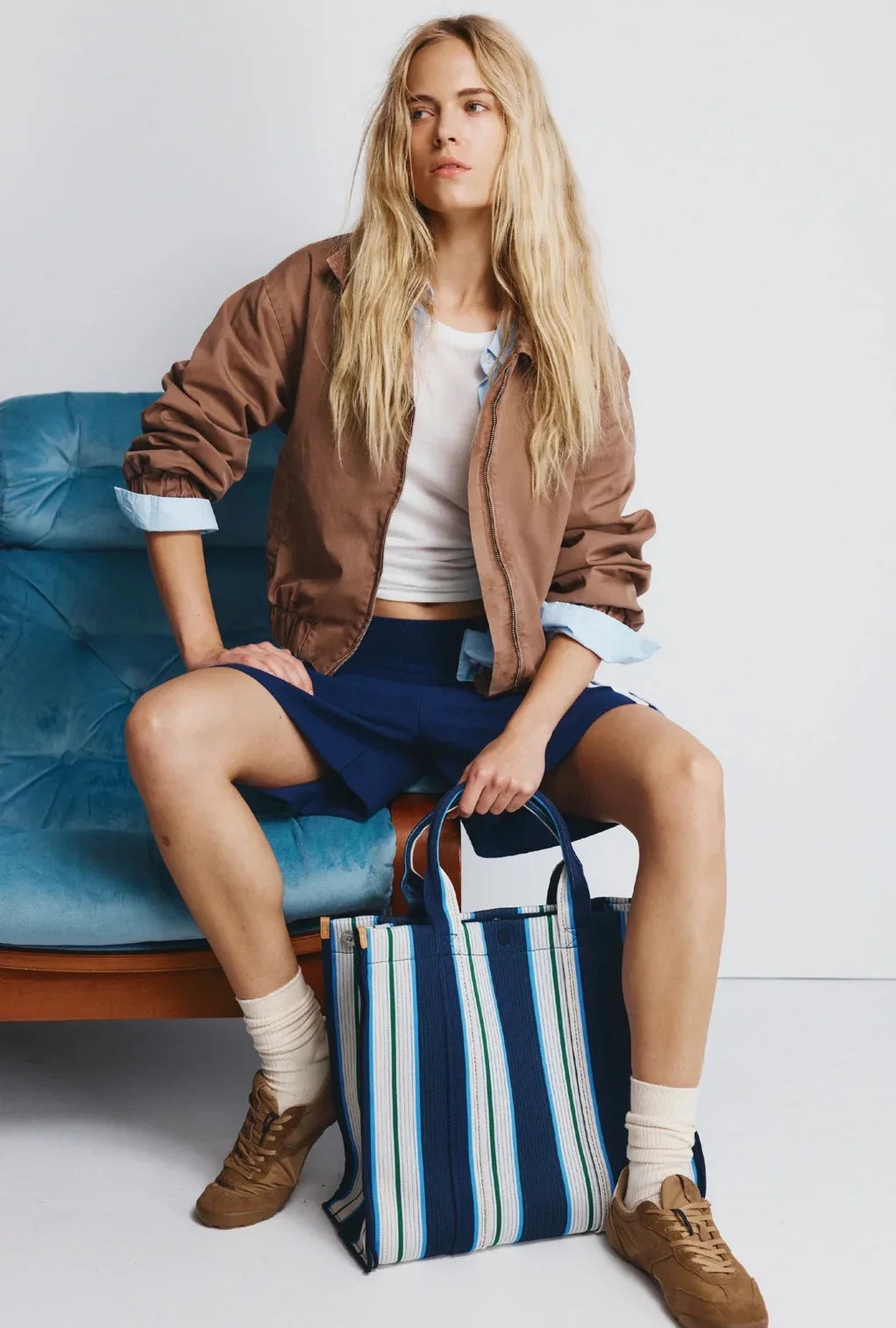 Woman in brown jacket and blue shorts holding striped tote bag, styled for casual fashion