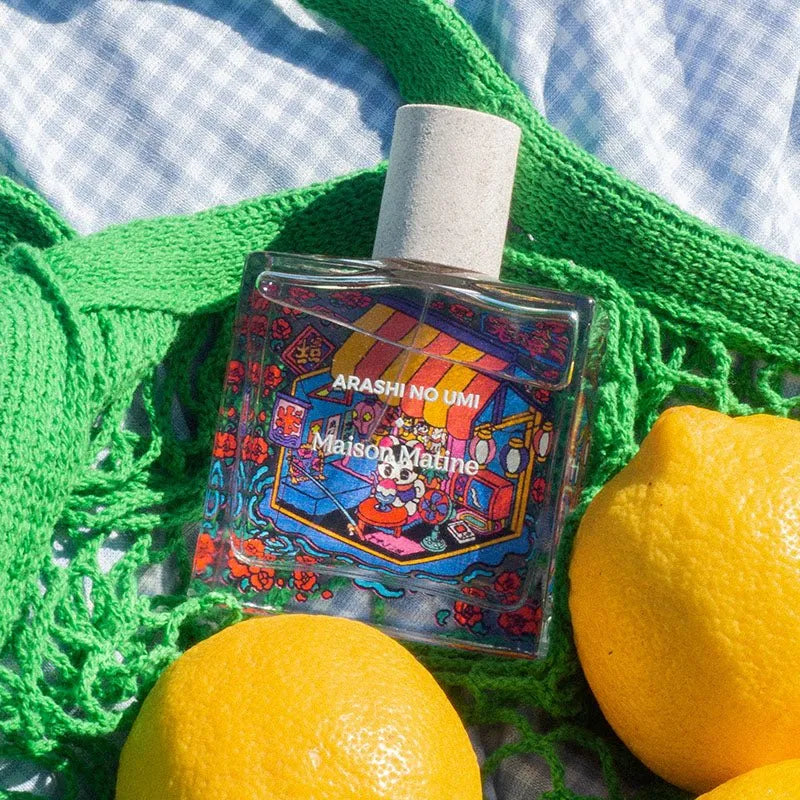 Maison Matine Arashi No Umi perfume bottle with vibrant label, nestled on green knit fabric beside fresh lemons