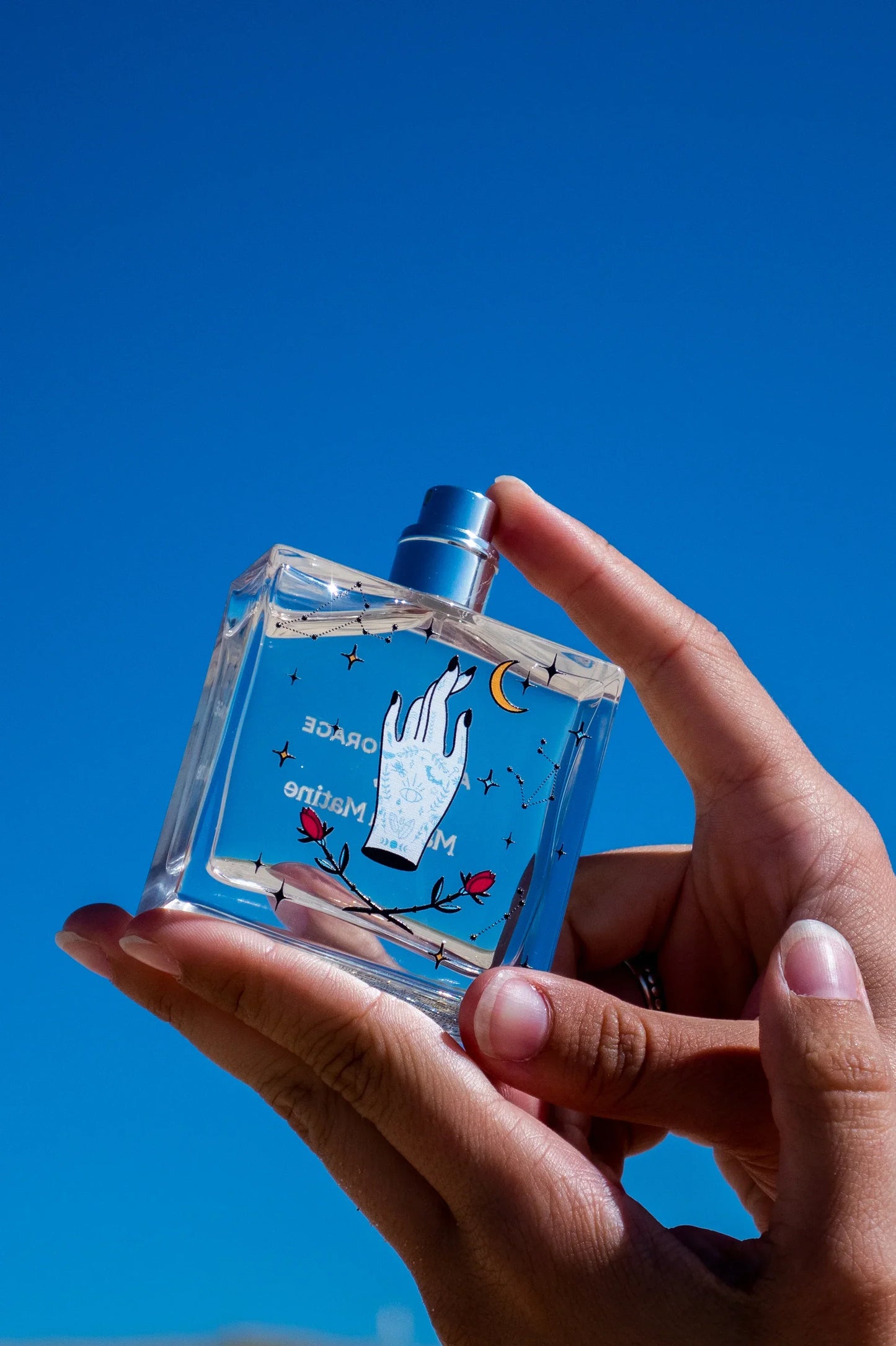 Hand holding blue perfume bottle with celestial design against clear sky