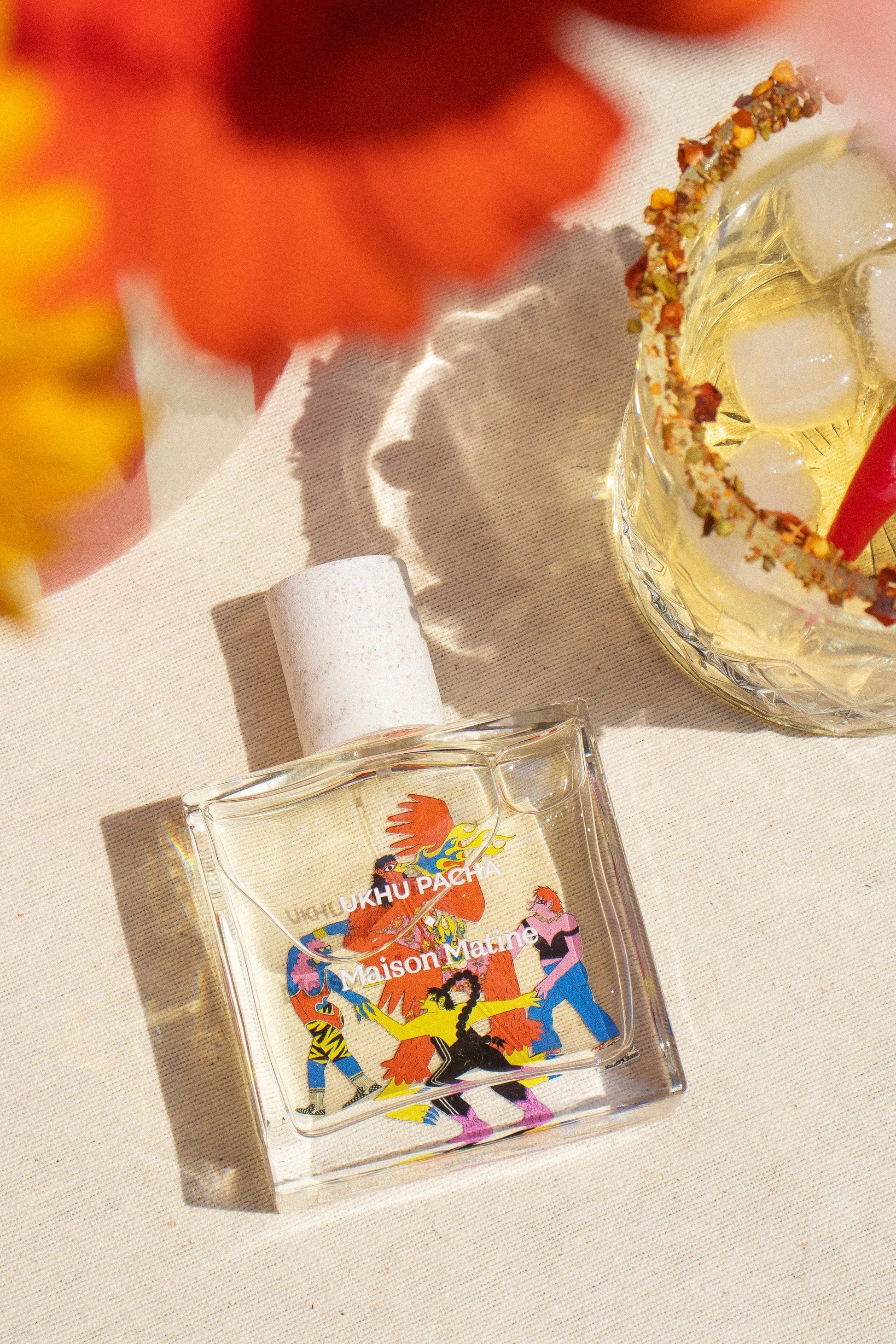 Maison Matine UKHU PACHA perfume bottle with vibrant label, beside spicy rimmed cocktail on linen, sunny aesthetic