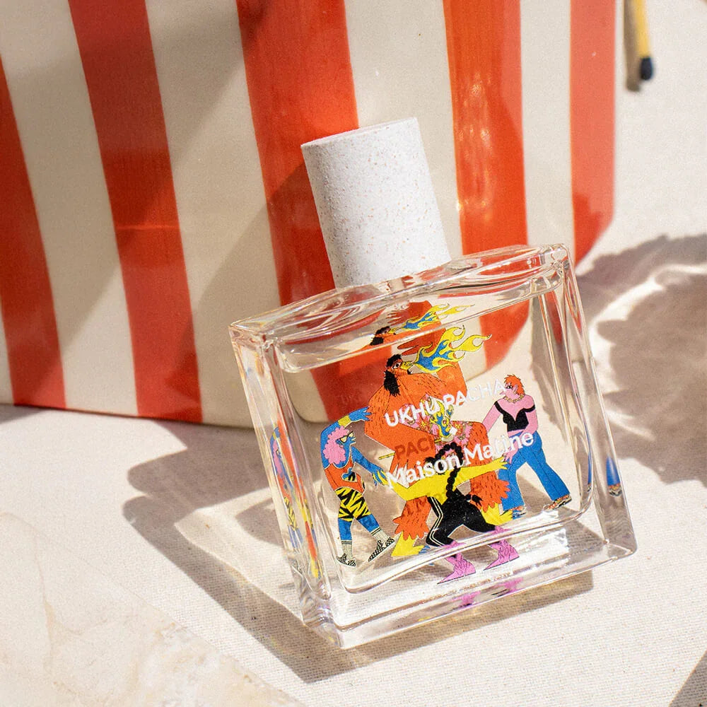 Clear glass perfume bottle with colorful illustrated characters, set against red and white stripes
