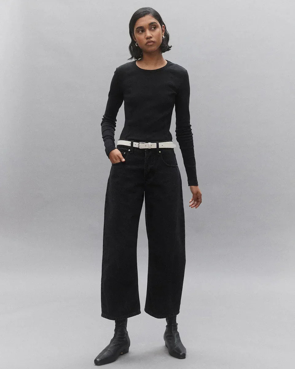 Woman in black long sleeve top, wide-leg jeans, white belt, and black ankle boots