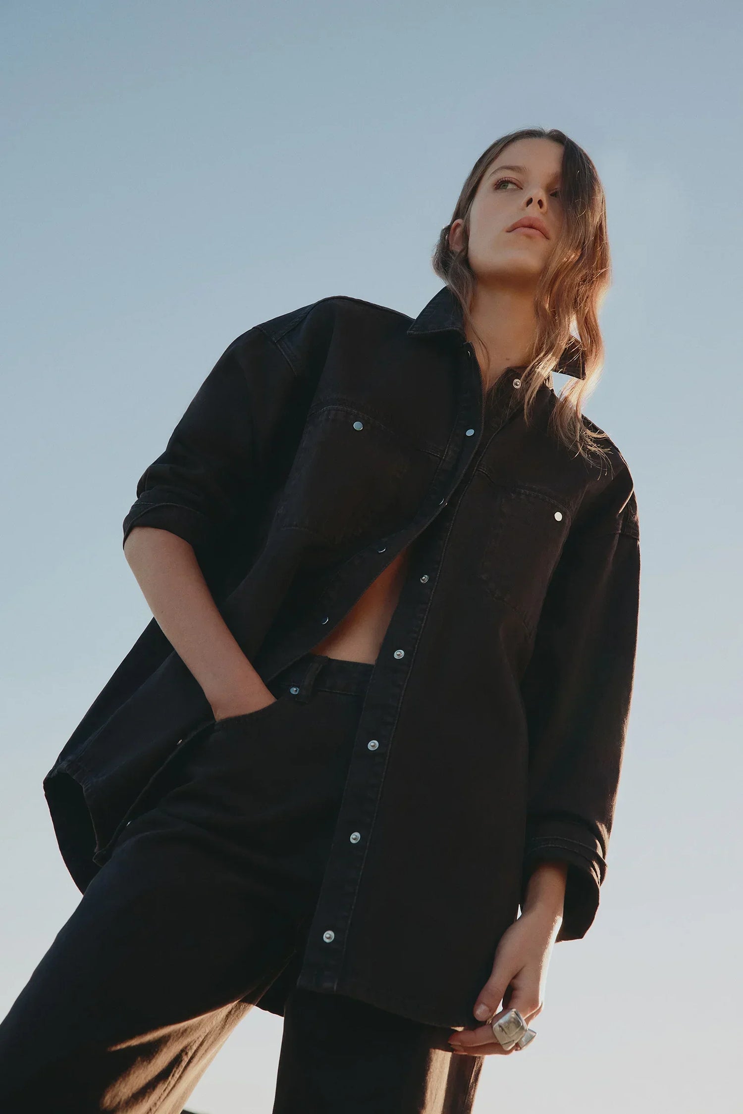 Woman in black oversized denim shirt and matching pants, stylish casual outfit against clear sky