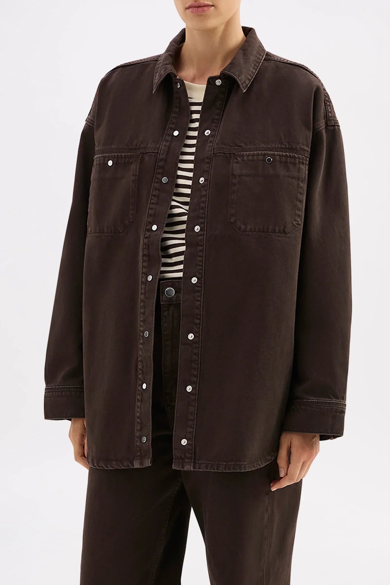 Dark brown oversized button-up shirt with chest pockets, styled over striped tee for casual chic look