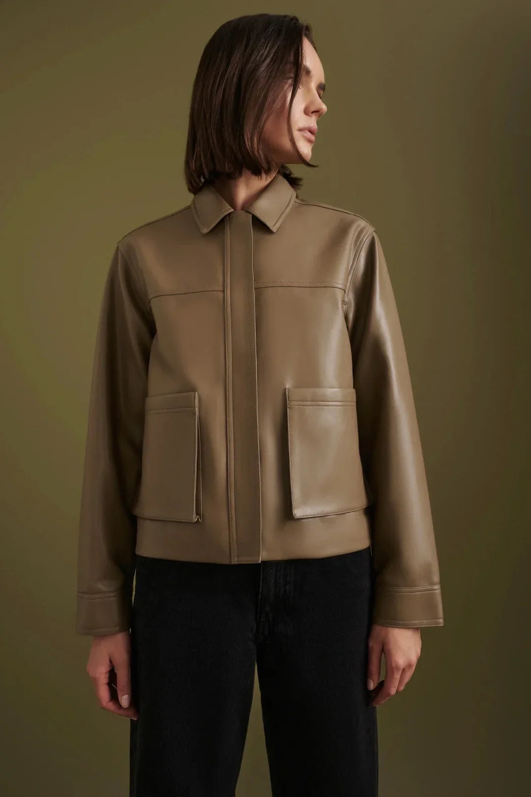 Women's olive green leather jacket with collar and front pockets, styled with black jeans