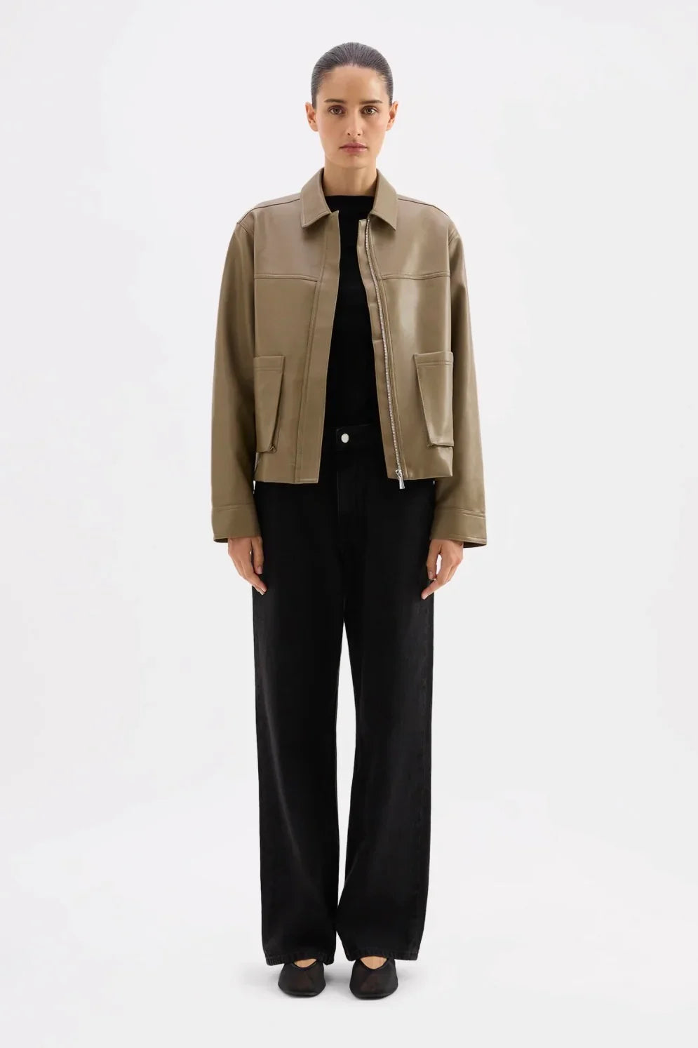 Women's olive green leather jacket with front pockets, styled with black wide-leg pants and flats
