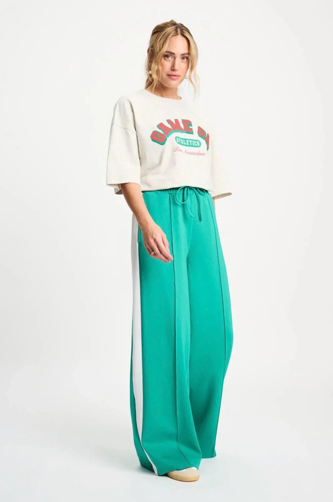 Woman in cream graphic tee and emerald green wide-leg pants with white side stripe, casual chic outfit