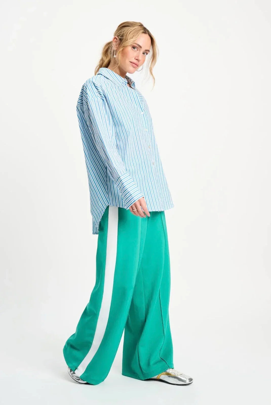 Woman in striped blue shirt and green wide-leg pants with white stripe, silver shoes