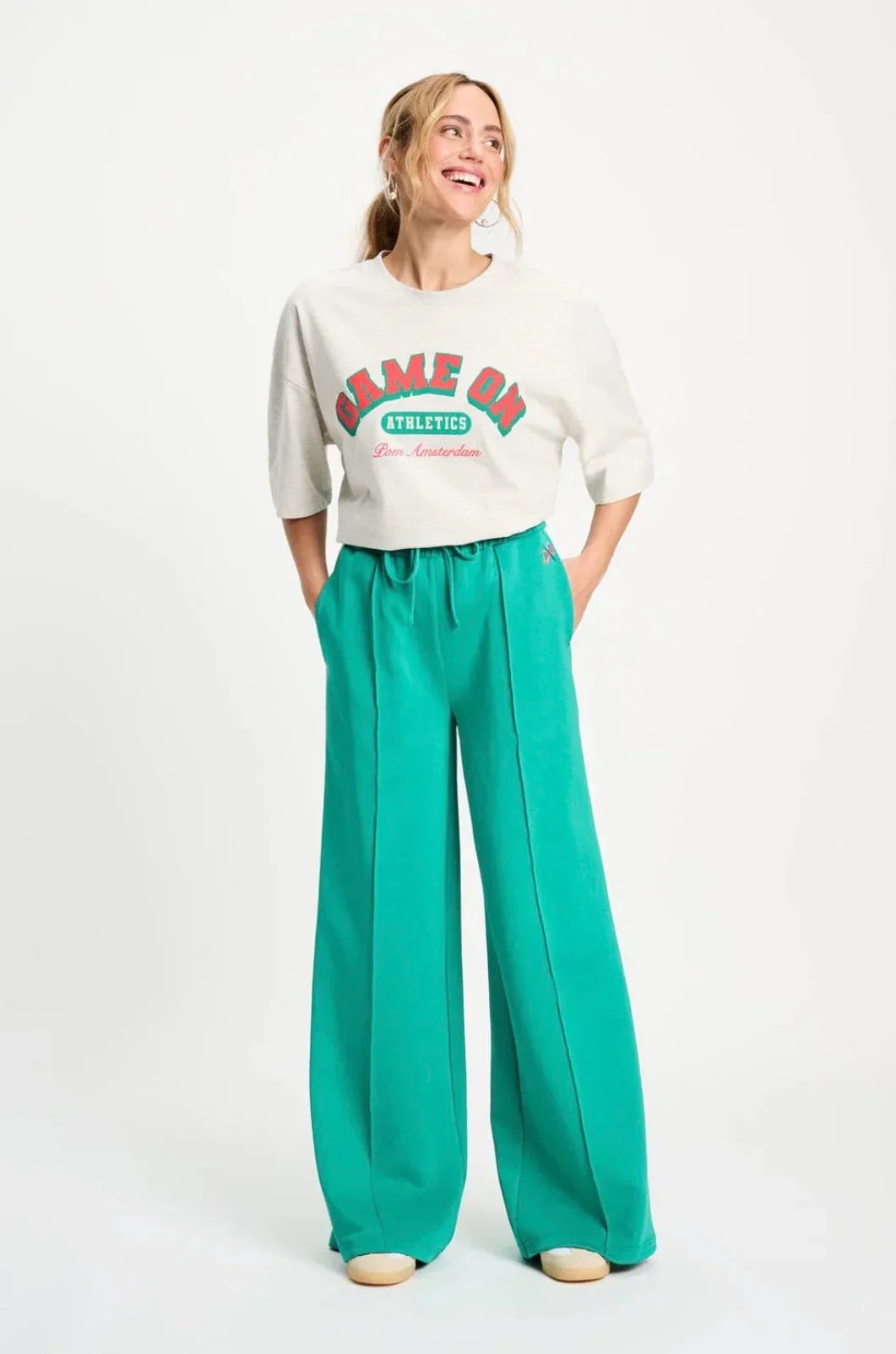 Woman in cream 'Game On Athletics' graphic tee and vibrant green wide-leg pants, stylish casual outfit