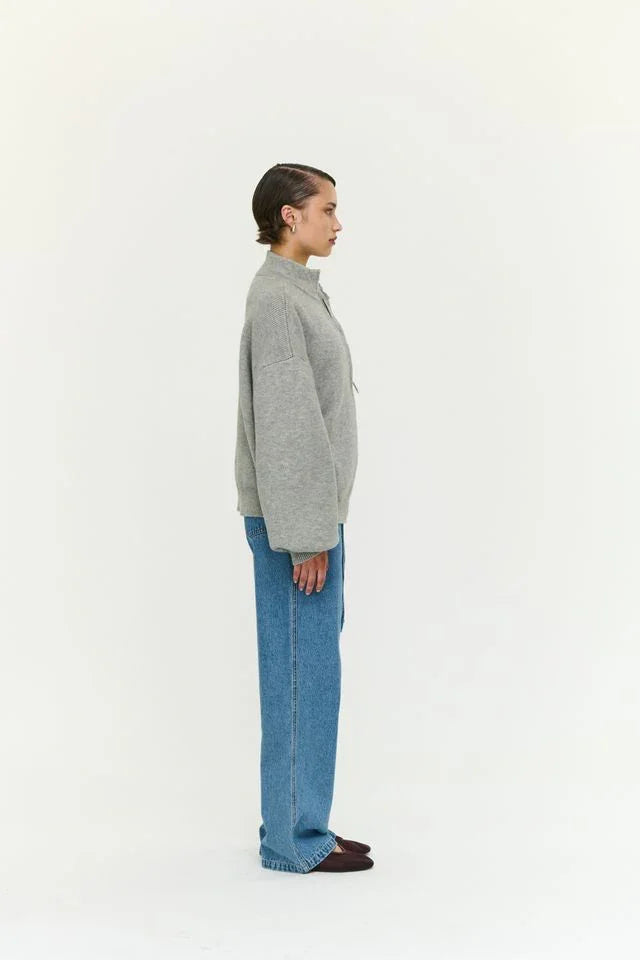 Woman in gray knit sweater and wide-leg blue jeans, side profile