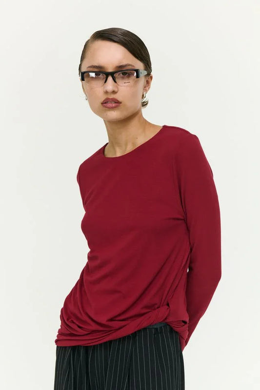 Woman wearing burgundy long sleeve top with twisted hem, paired with black pinstripe pants, modern minimalist style
