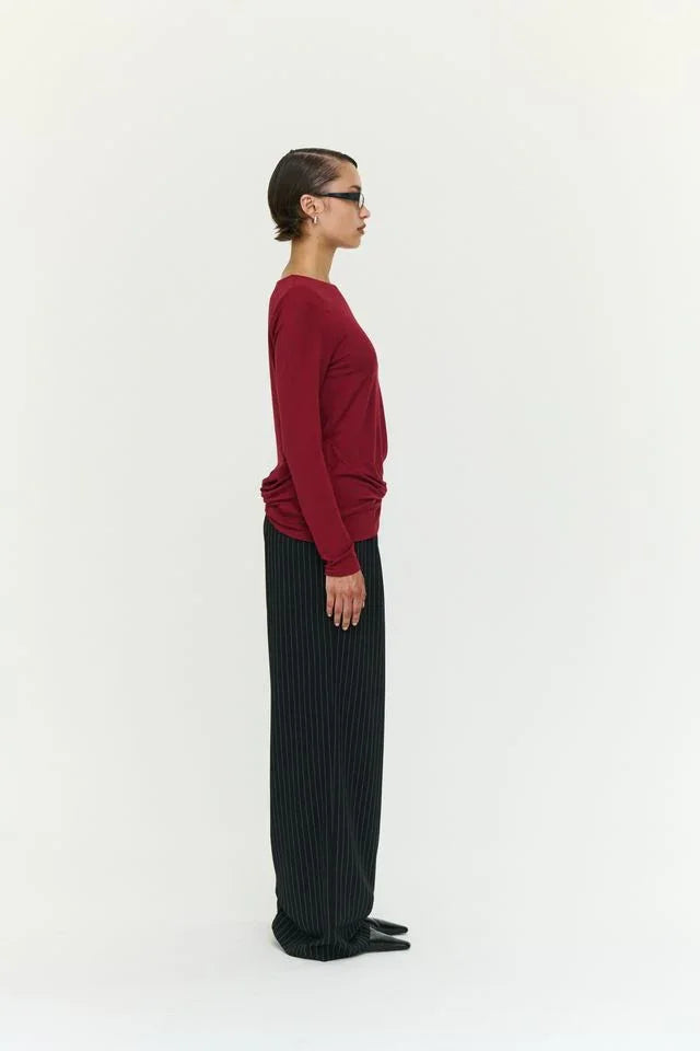 Woman in burgundy long-sleeve top and black pinstripe pants, side profile