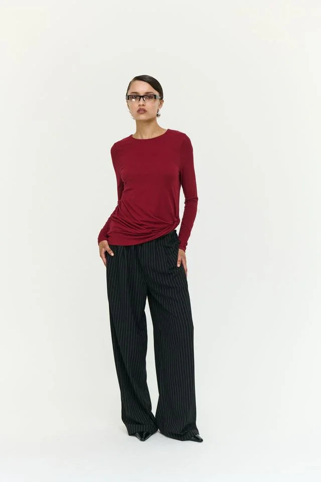 Woman in burgundy long sleeve top and black pinstripe wide-leg pants, modern women's fashion