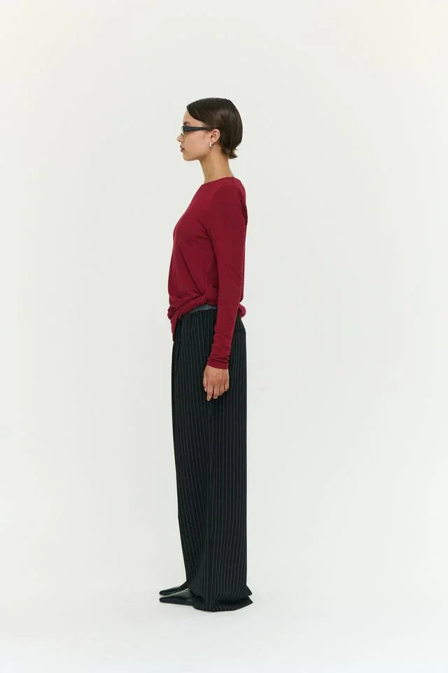 Woman in burgundy long-sleeve top and black pinstripe wide-leg pants, side profile